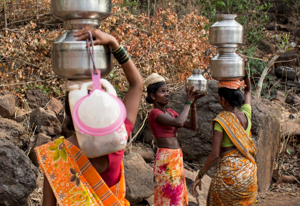 A woman helps another in carrying metal pitchers filled with water from a well outside Denganmal village, Maharashtra, India, April 20, 2015. In Denganmal, a village in Maharashtra state, some men take a second or third wife just to make sure their households have enough drinking water. Becoming what are known as 