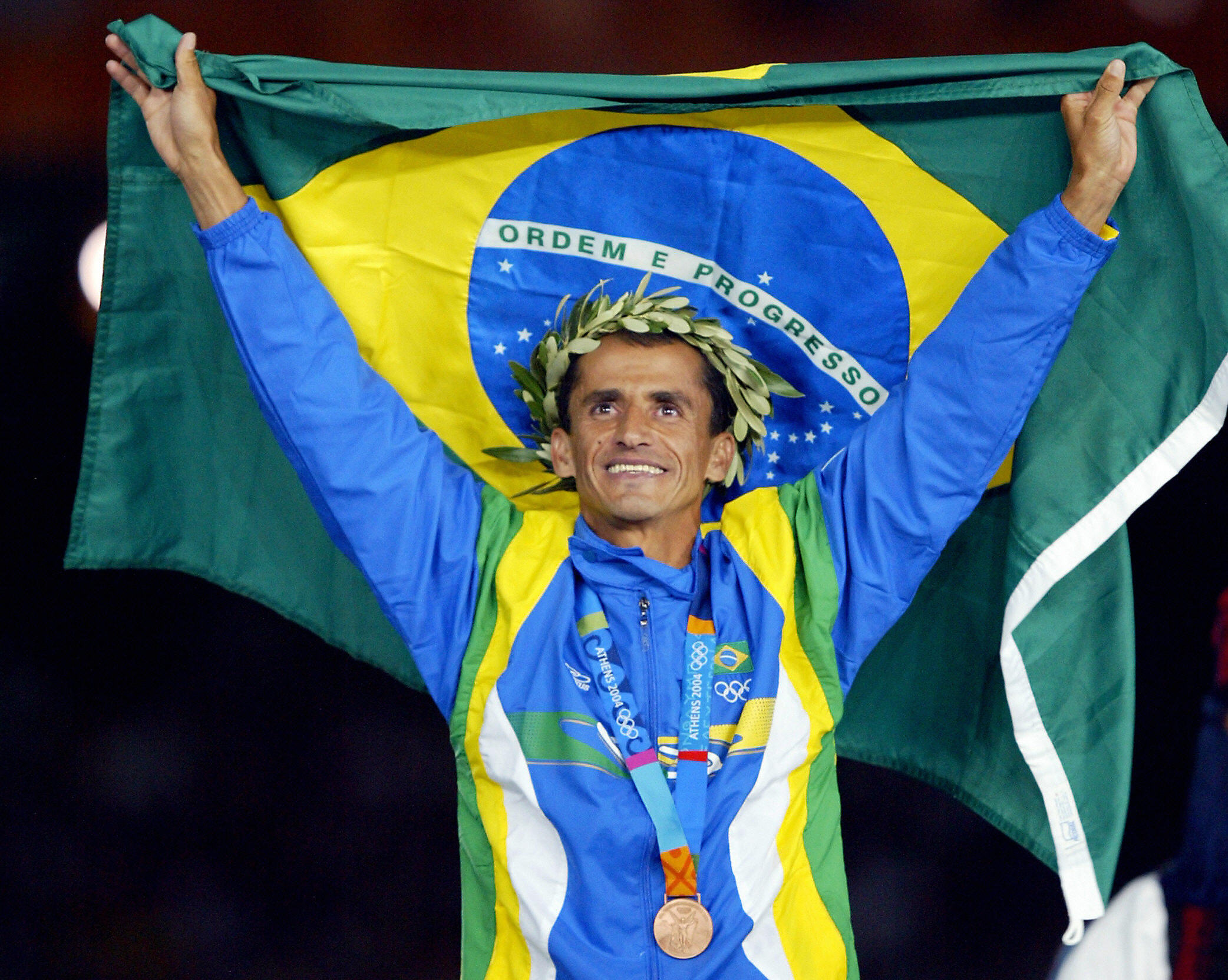 ATHENS, Greece: Men's marathon bronze medal winner Vanderlei de Lima of Brazil stands on the winners' podium 29 August 2004, during the Olympic Games medals ceremony at the Olympic Stadium in Athens. Long-time race leader de Lima was attacked by a spectator in the latter stages of the race but recovered and hung on to win the bronze while Stefano Baldini of Italy won the gold and Mebrahtom Keflezighi of the US took the silver. AFP PHOTO/ADRIAN DENNIS (Photo credit should read ADRIAN DENNIS/AFP/Getty Images)