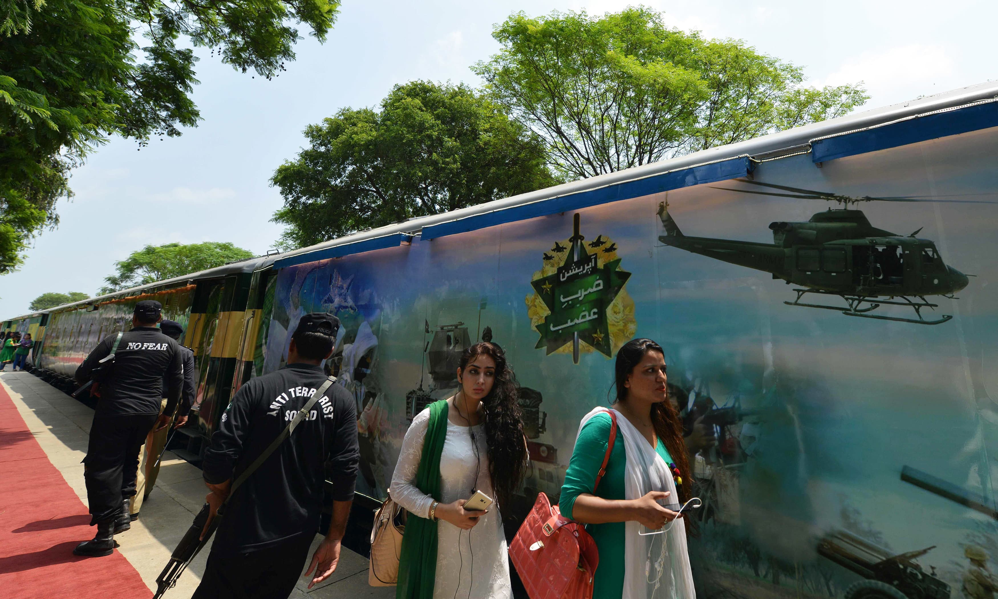Pakistani policemen and residents walk past carriages of the 'Azadi Train' (Independence Train)before its journey from Margalla Railway Station in Islamabad on August 11, 2016, ahead of Independence Day celebrations. The train consists of coaches representing the culture and traditions of all four provinces of Pakistan and Pakistan-administered Kashmir and is scheduled to cover some 4,000 kms in a journey of a month which will culminate in the port city of Karachi. Pakistan celebrates the 69th anniversary of the country's independence from British rule on August 14. / AFP PHOTO / AAMIR QURESHI